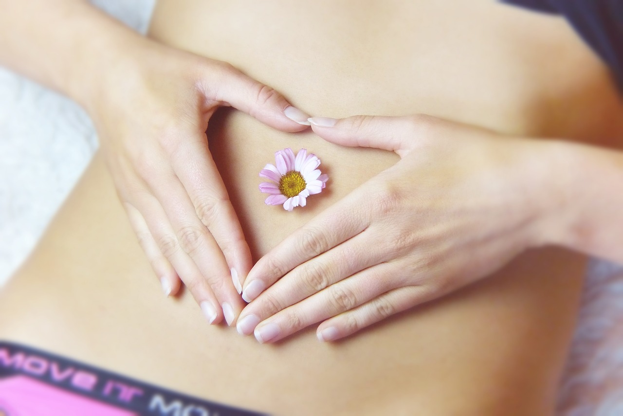 Picture of a woman's belly with her hands in the shape of a heart with a little flower showing that your digestive system is in need of byōm™️. 